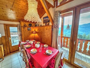 A dining area with a red tablecloth, wooden walls, and a view of the sea through large windows. - Chalet La Chiserette is a cosy traditional style chalet for 8/10 people (Peisey Vallandry)