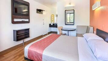 A hotel room with a bed, a TV mounted on the wall, a small table, and a chair.