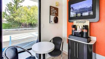 A coffee station with a sign indicating a morning charge for no charge, a television screen, and a view of the outside.
