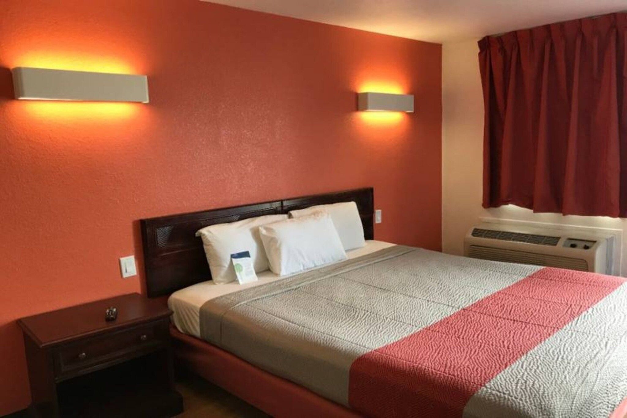 A hotel room with a bed, nightstands, a heater, and a window with curtains.