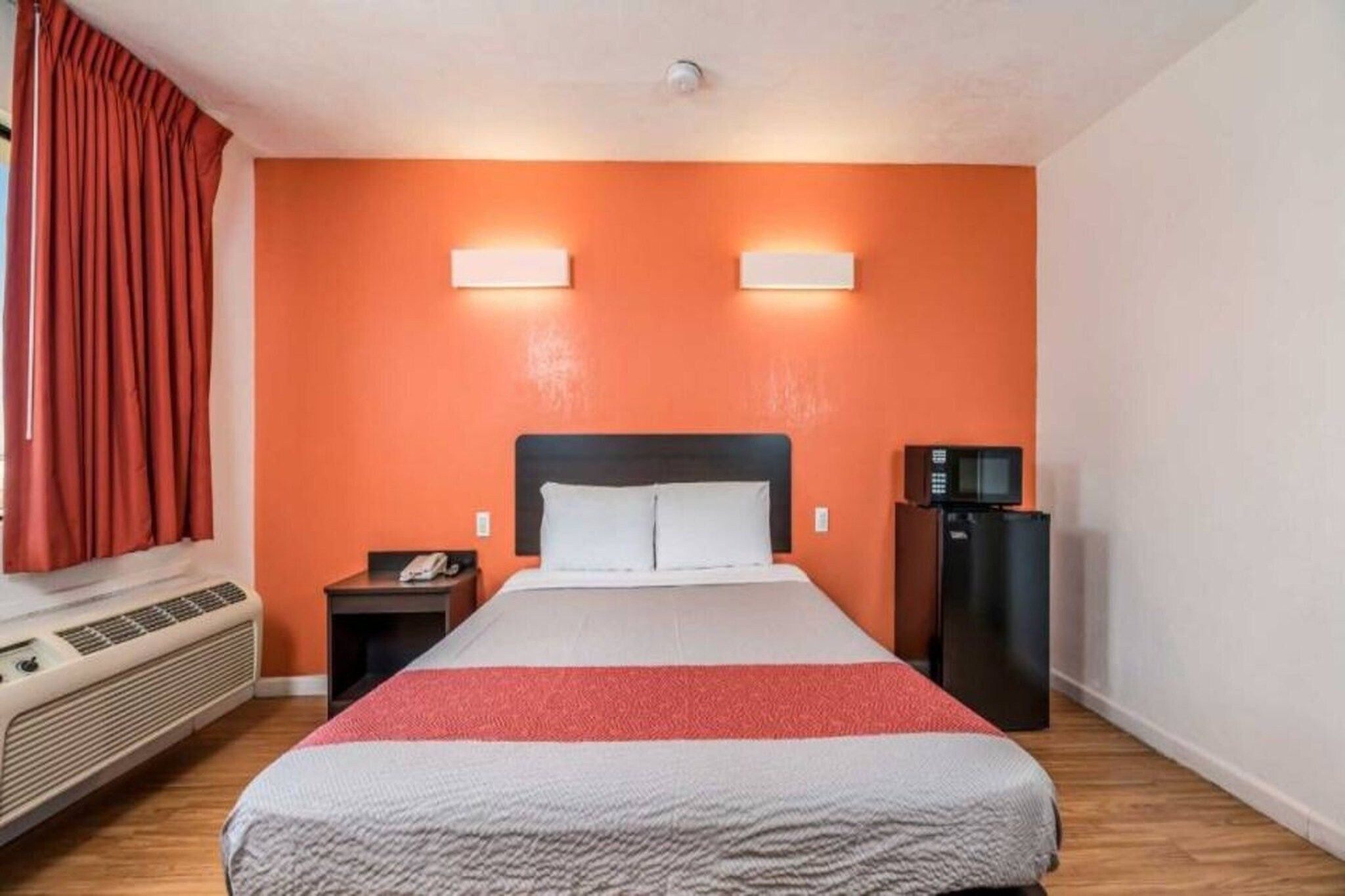 A hotel room with a bed, a nightstand, a telephone, a microwave, and a heater.