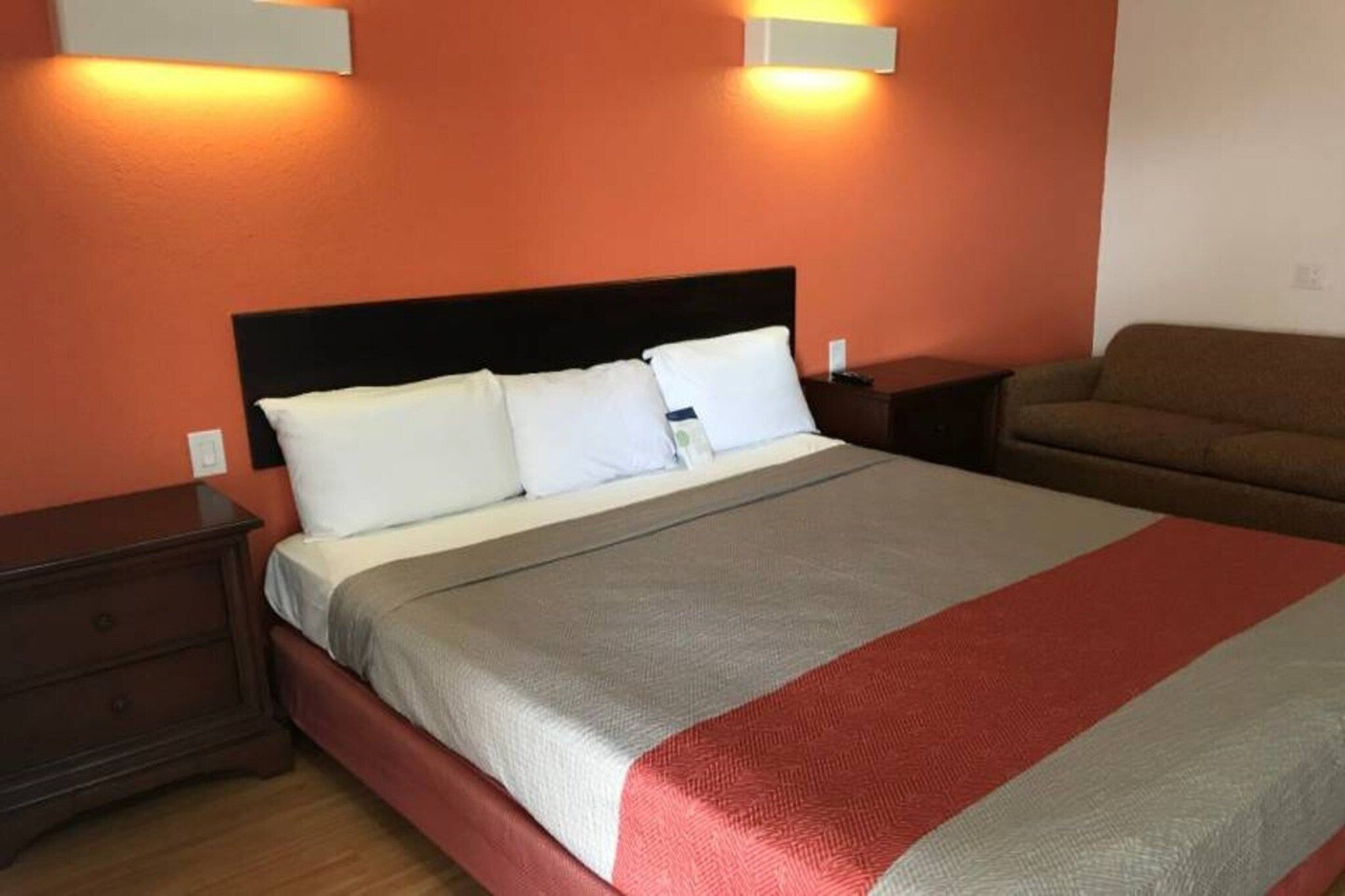 A hotel room with a bed, a nightstand, a dresser, and a sofa.