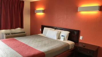 A hotel room with a bed, a nightstand, a wall-mounted heater, and a window with curtains.