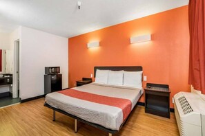 A hotel room with a bed, bedside tables, a heater, and a small kitchenette with a microwave.