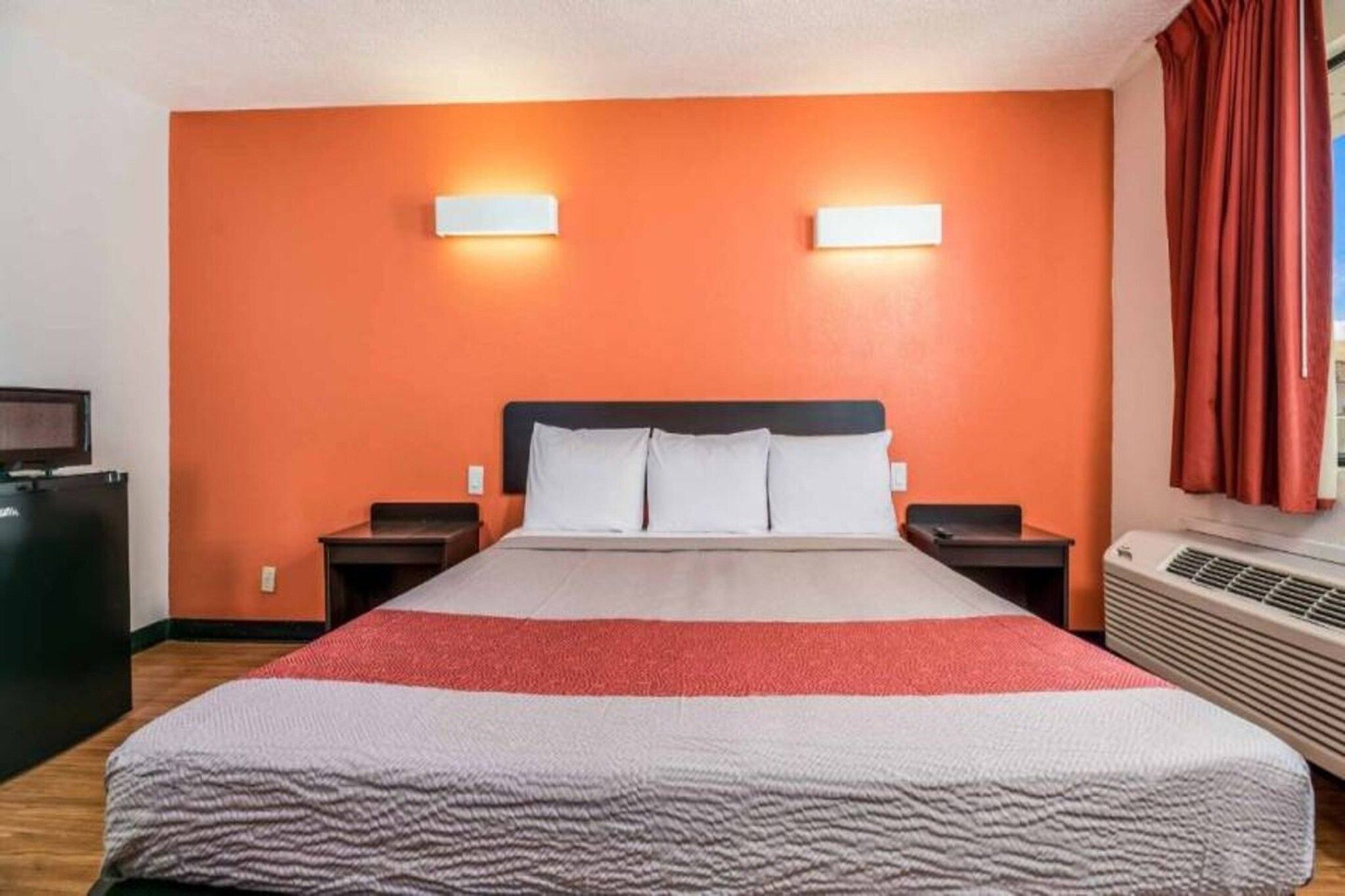 Ein Hotelzimmer mit einem großen Bett, zwei Nachttischen, einem Flachbildfernseher und einer Klimaanlage.