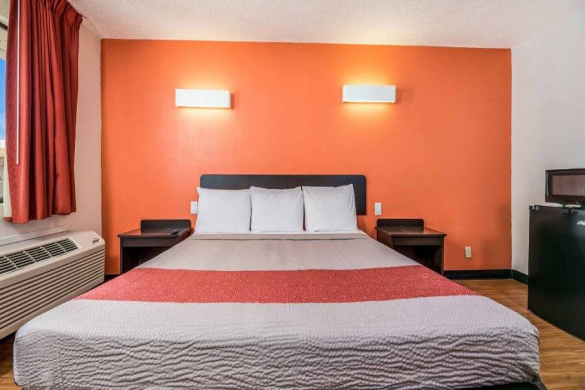 A hotel room with a bed, two bedside tables, a TV, and a wall-mounted heater.