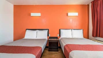 A hotel room with two beds, a wooden floor, and orange walls.