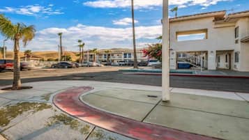 A street view with a curved sidewalk, palm trees, and a row of buildings with a parking area.