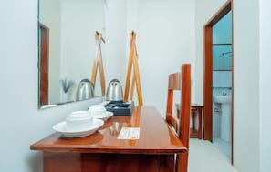 A dining area with a wooden table, white plates, a kettle, and a remote control. - Hotel Alexander (Puerto Princesa)