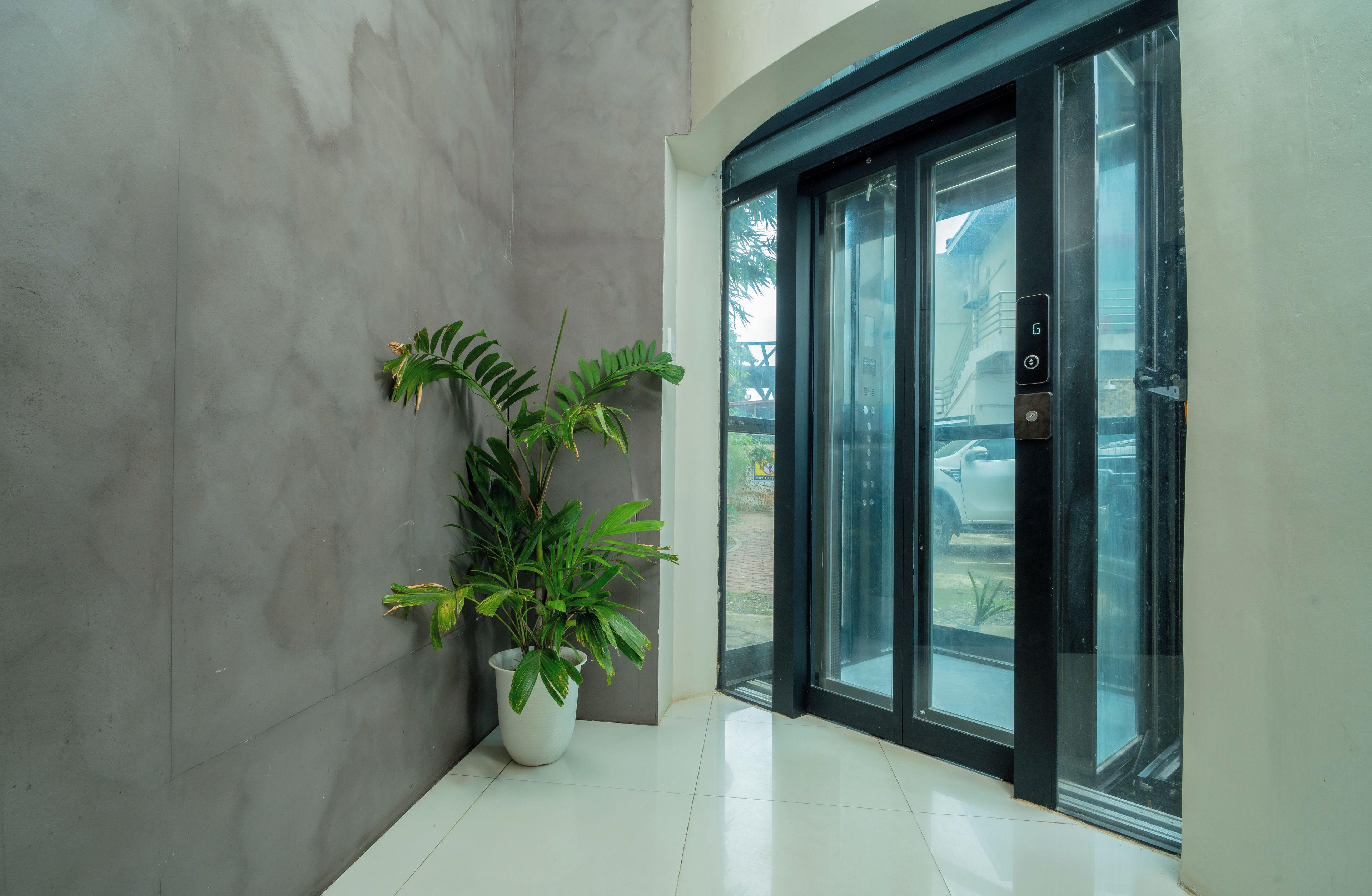 A modern building entrance with a potted plant, a glass door, and a digital display.