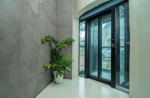A modern building entrance with a potted plant, a glass door, and a digital display. - Hotel Alexander (Puerto Princesa)