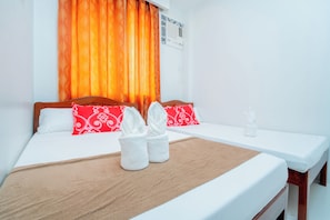 A hotel room with a bed, two pillows, a bedside table, and a window with curtains. - Hotel Alexander (Puerto Princesa)