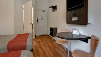 A room with a bed, a table with chairs, a television mounted on the wall, and a door leading to another room.