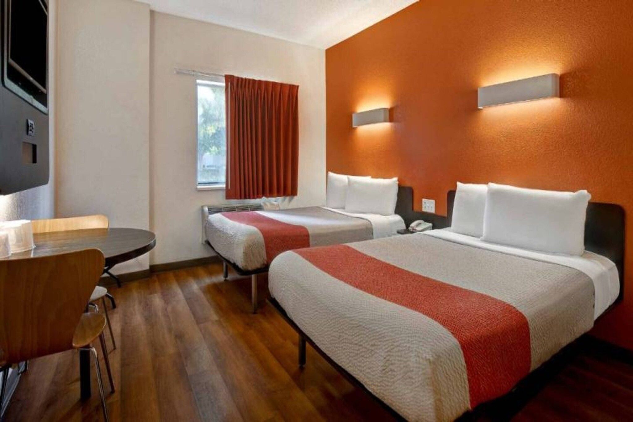 A hotel room with two beds, a desk, and a window with curtains.