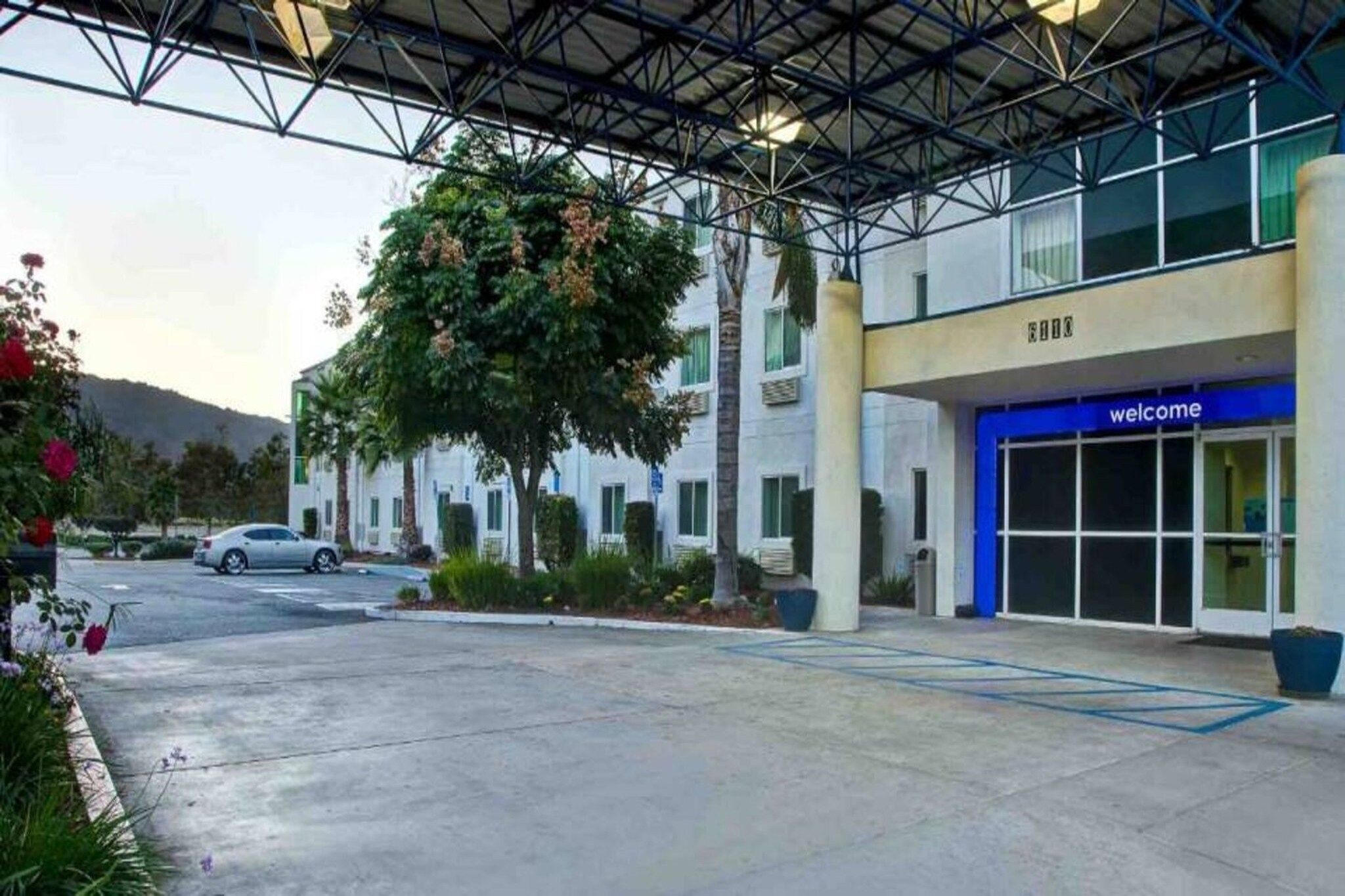 A hotel entrance with a covered walkway, a 'welcome' sign, and a parking area.