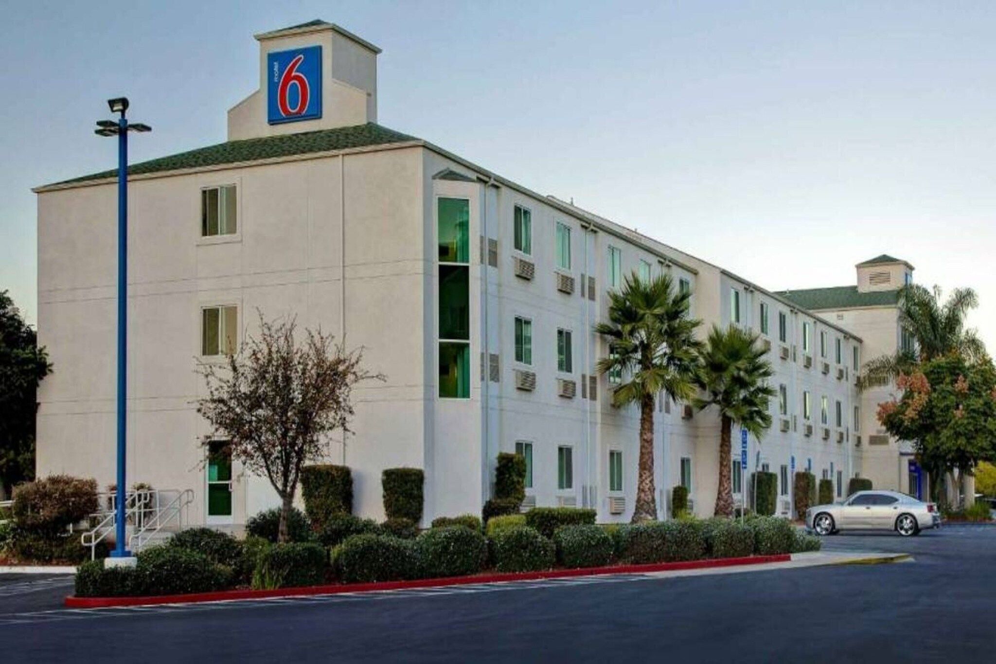 A 6-story hotel with a flat facade, multiple windows, and a parking lot with a single car.