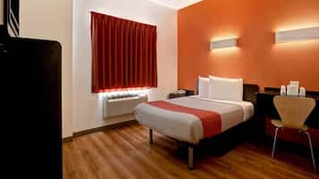 A hotel room with a bed, a desk, a chair, an air conditioning unit, and a window with curtains.