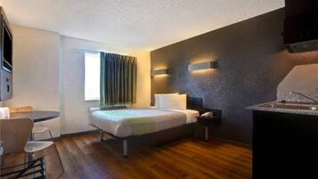 A compact hotel room with a bed, bedside table, and a small kitchenette.