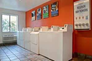 A laundry area with four washing machines, a window with a view, and a wall with detergent advertisements. - Cozy King Bed Room|Fridge|Free WiFi (Gilroy)