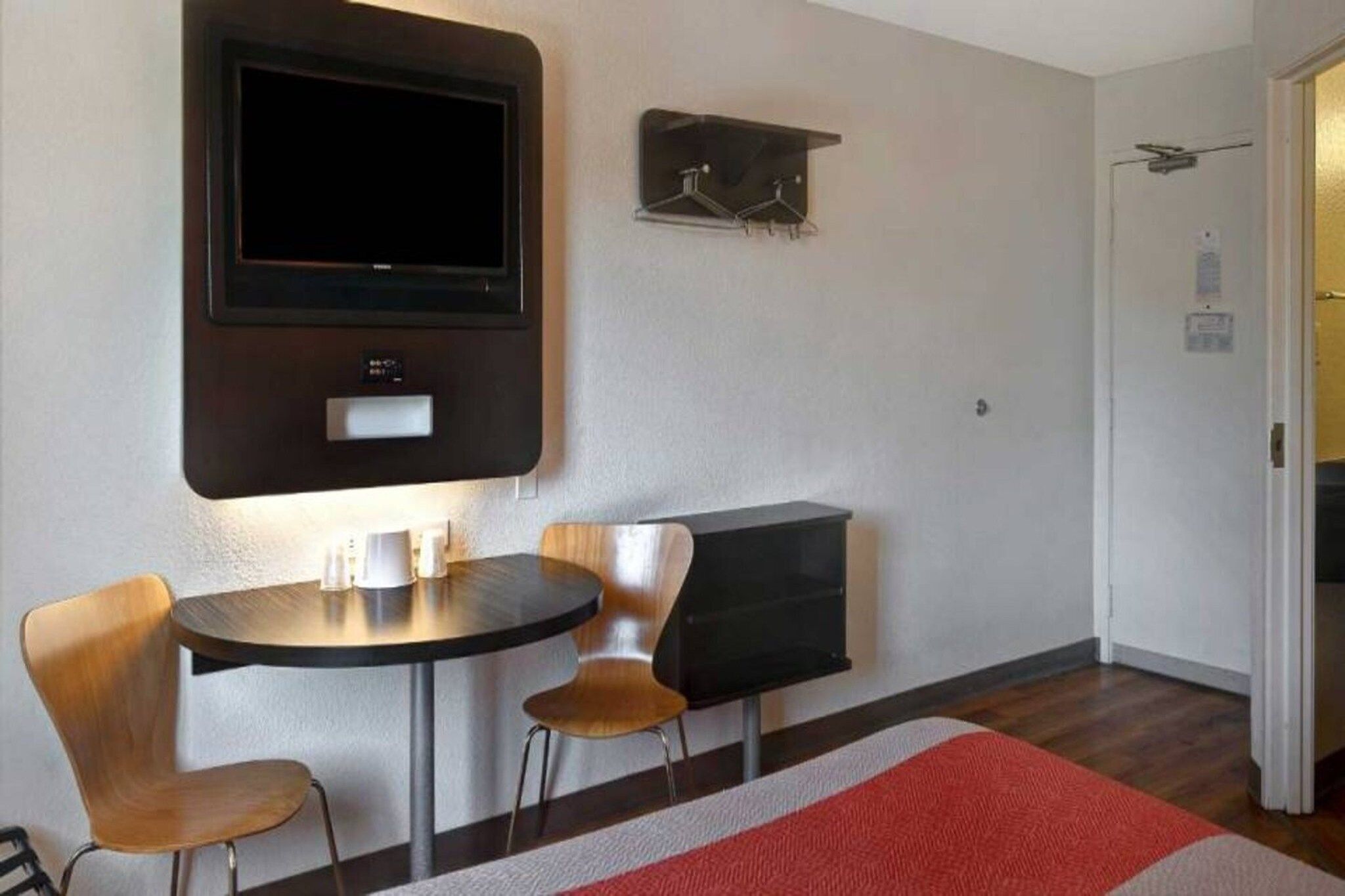 A room with a flat-screen TV mounted on the wall, a small table with two chairs, and a coat rack with hangers.