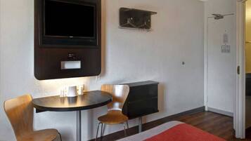 A room with a flat-screen TV mounted on the wall, a small table with two chairs, and a coat rack with hangers.