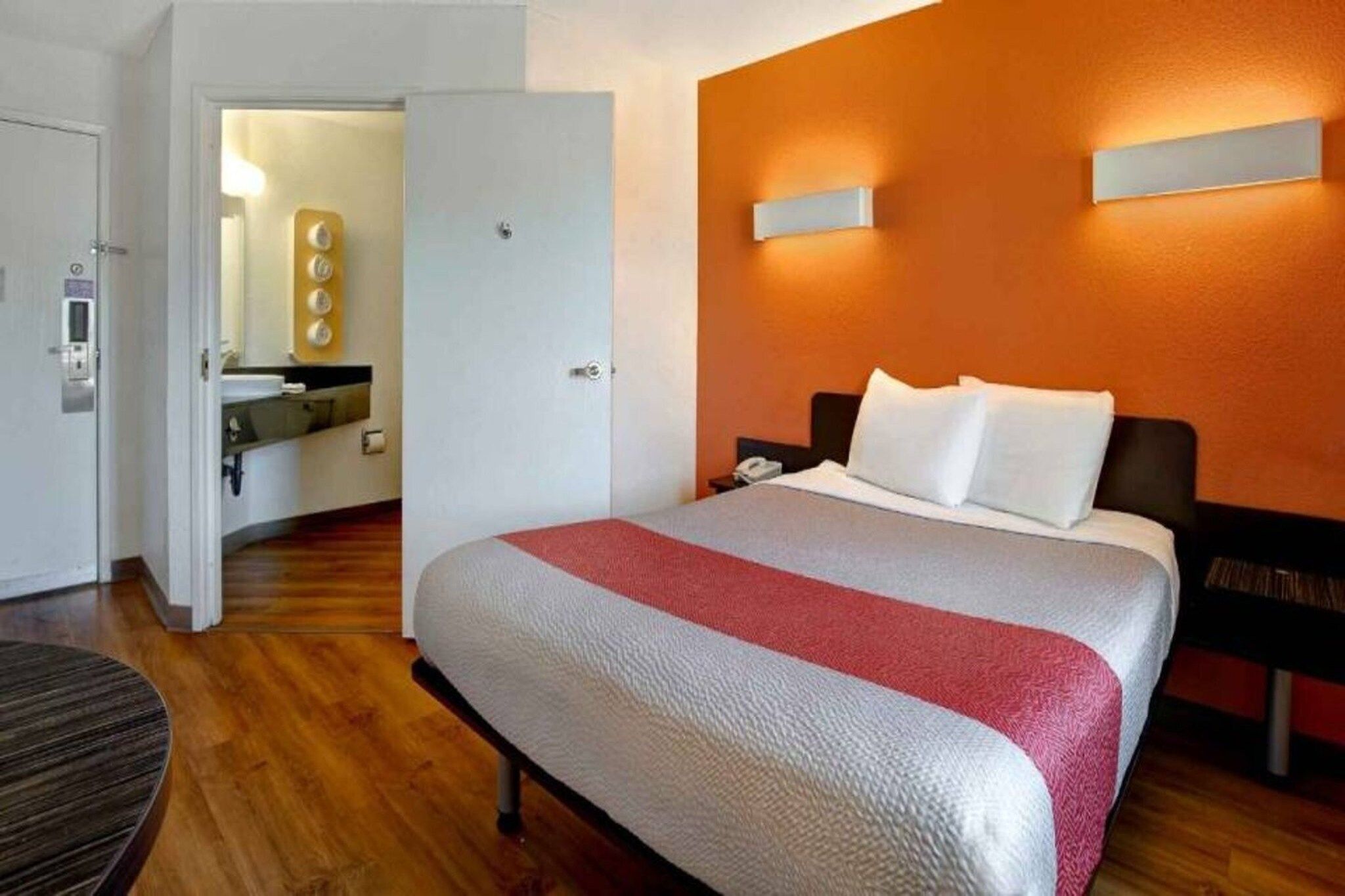 Ein Hotelzimmer mit einem Bett, einem Nachttisch, einem Schreibtisch mit Telefon und einem durchgehenden Türspalt sichtbaren Badezimmer.