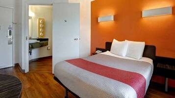 Ein Hotelzimmer mit einem Bett, einem Nachttisch, einem Schreibtisch mit Telefon und einem durchgehenden Türspalt sichtbaren Badezimmer.