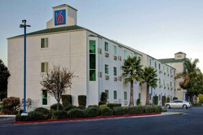 A 6-story hotel with a flat facade, multiple windows, and a parking lot with a single car.