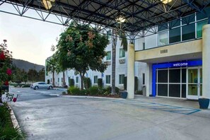 Entrada d'hotel amb una galeria coberta, un rètol de 'welcome' i una zona d'aparcament.