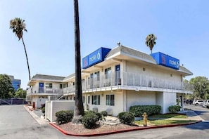 A motel with a two-story structure, a balcony on the second floor, and a parking lot in the foreground.