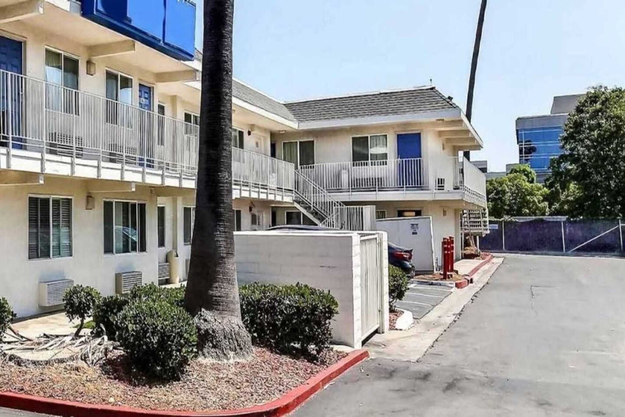 Motel de dues plantes amb aparcament, una palmera i una petita zona de jardí.