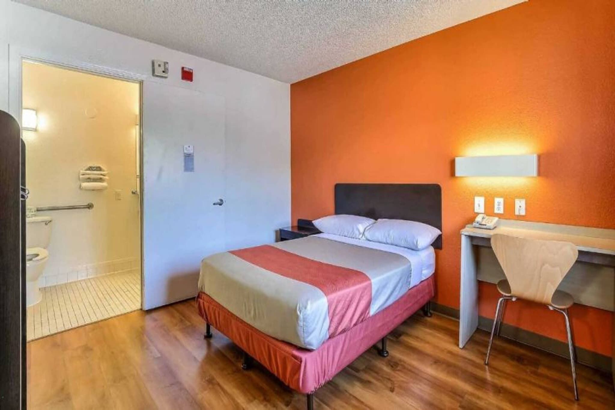 A hotel room with a bed, a desk, a chair, and a bathroom.