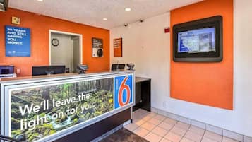 Zona de recepció d'hotel amb una pantalla digital que mostra un mapa, un rellotge i un cartell que diu 'Deixarem la llum encès per tu'.