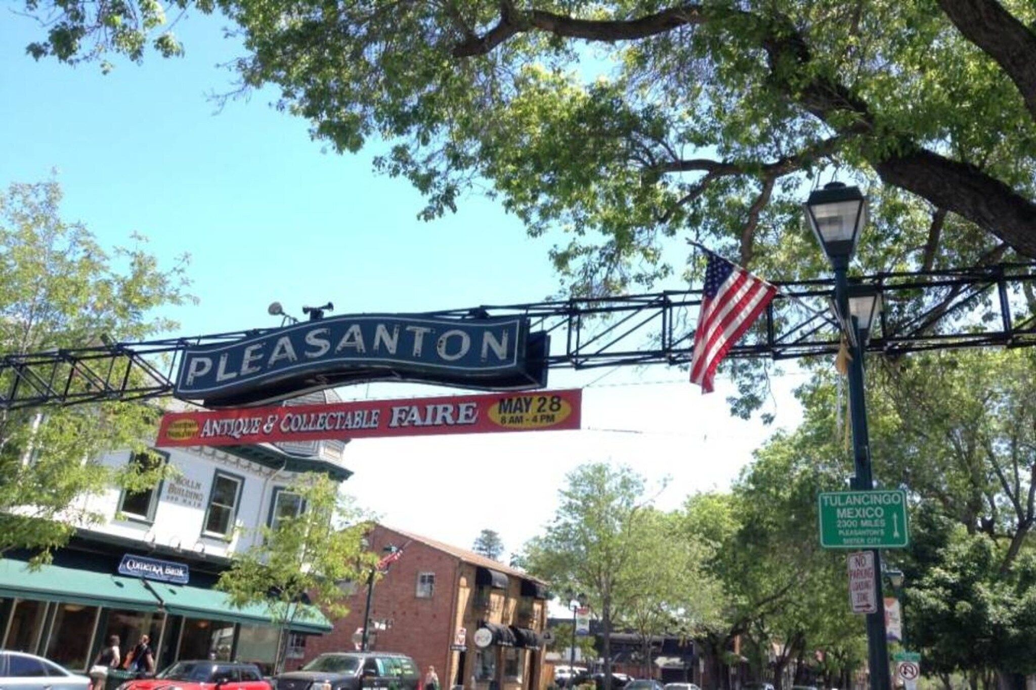 Un panneau de signalisation indiquant la ville de Pleasanton, avec un drapeau américain et un panneau annonçant une foire d'antiquités et d'objets de collection.
