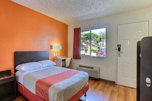 A hotel room with a bed, a desk, a window with a view of the outside, and a door.