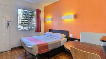 Quarto de hotel com cama, escrivaninha e cadeira. Janela com vista para edifícios.