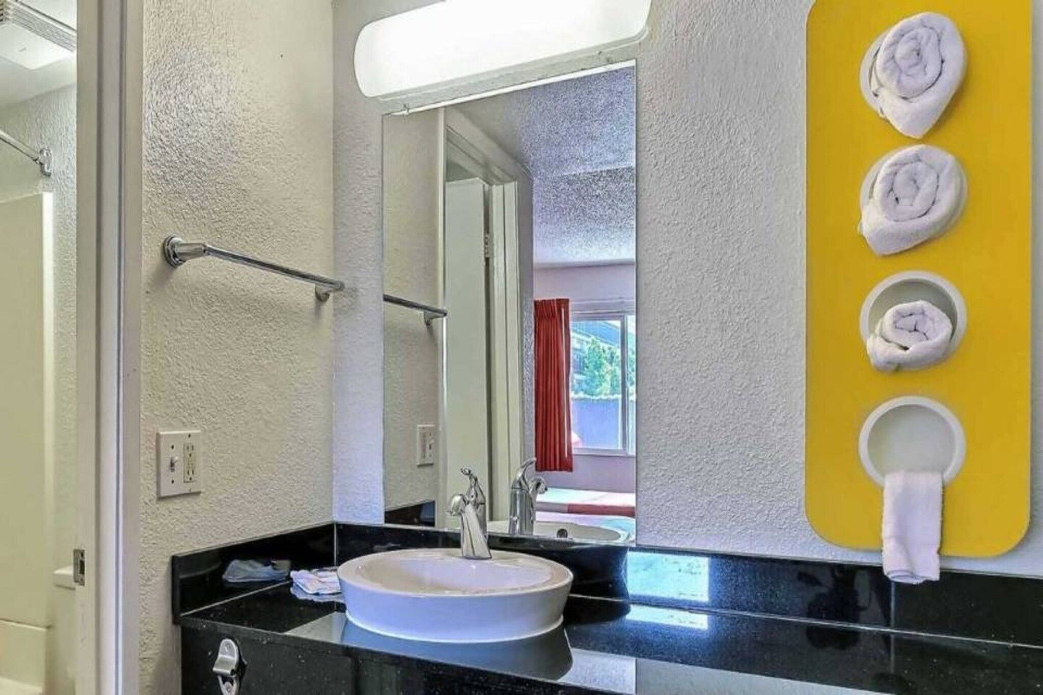 Ett badrum med handfat, spegel, handdukshängare och en gul handduksdispenser.
