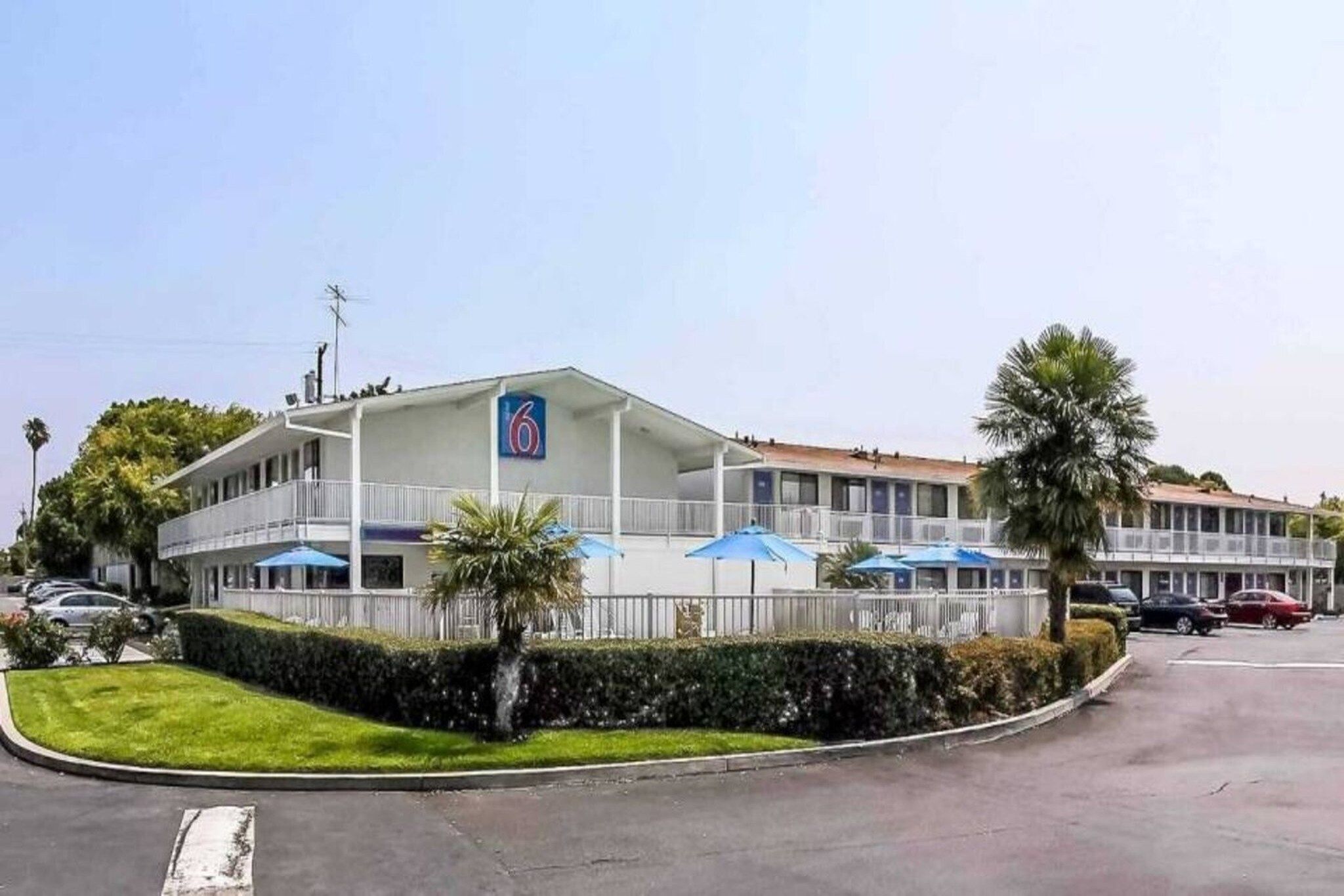 A motel with a prominent '6' sign, a covered outdoor seating area, and a parking lot.