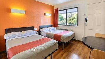 A hotel room with two beds, a dining table, and a window with a view of trees.