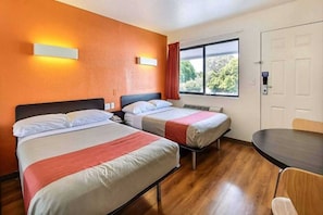 Une chambre d’hôtel avec deux lits, une table à manger et une fenêtre donnant sur des arbres.