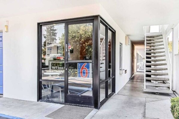 Ingresso di un hotel con porta in vetro, cartello che indica la stanza numero 6, e una scala a destra.