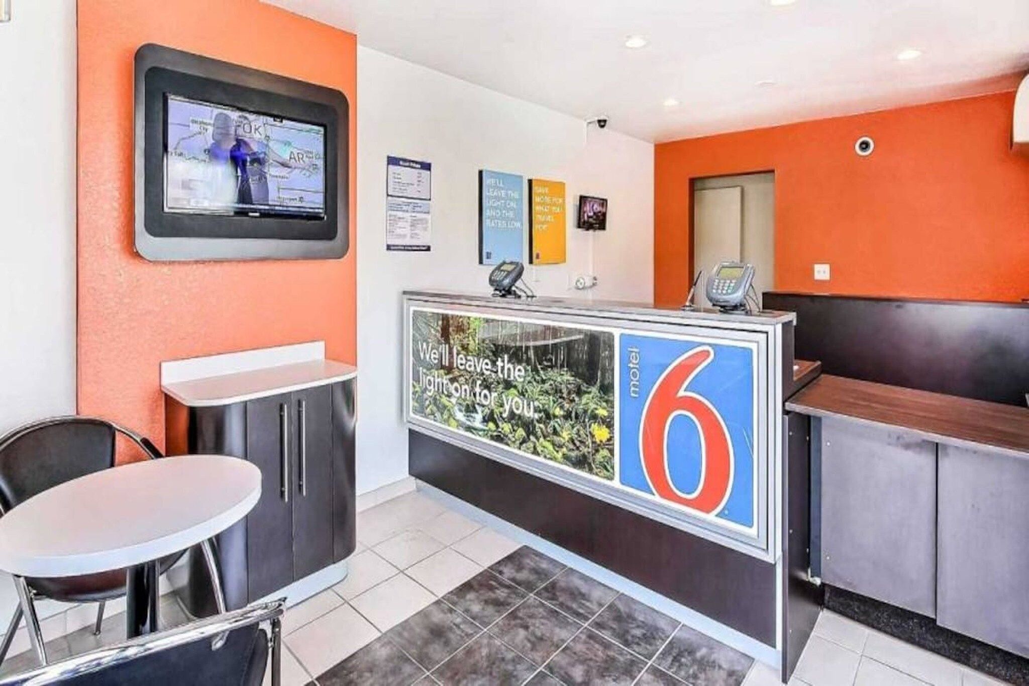 A hotel reception area with a counter, seating, and a television screen.