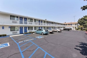 Un motel con diverse camere, un parcheggio senza indicazioni per l'afflusione e un cielo sereno.