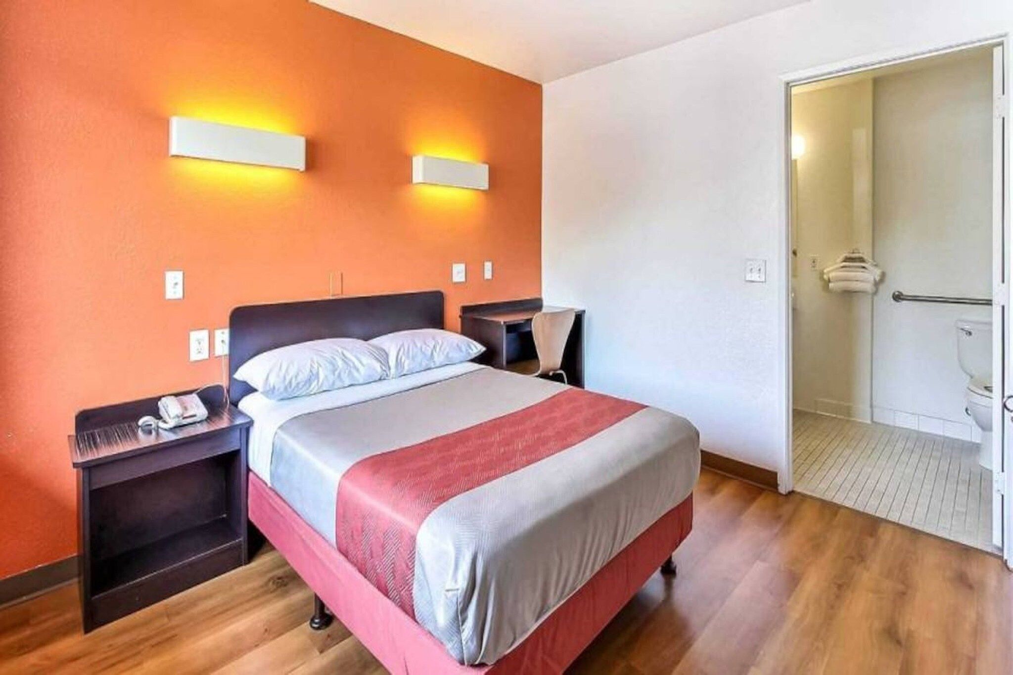 Una habitación de hotel con cama, mesitas de noche, un escritorio y un espacio para la ducha.