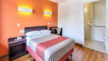 Una habitación de hotel con cama, mesitas de noche, un escritorio y un espacio para la ducha.