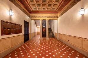 A hallway with patterned flooring, a wooden cabinet with nameplates, and a staircase leading to an upper level. - Tuscan Gold by MMega (Firenze)