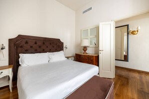 A hotel room with a large bed, a wooden nightstand, a dresser, a mirror, and a door. - Tuscan Gold by MMega (Firenze)