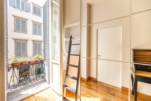 A room with a wooden floor, a ladder, and a view of a balcony with potted plants. - Tuscan Gold by MMega (Firenze)