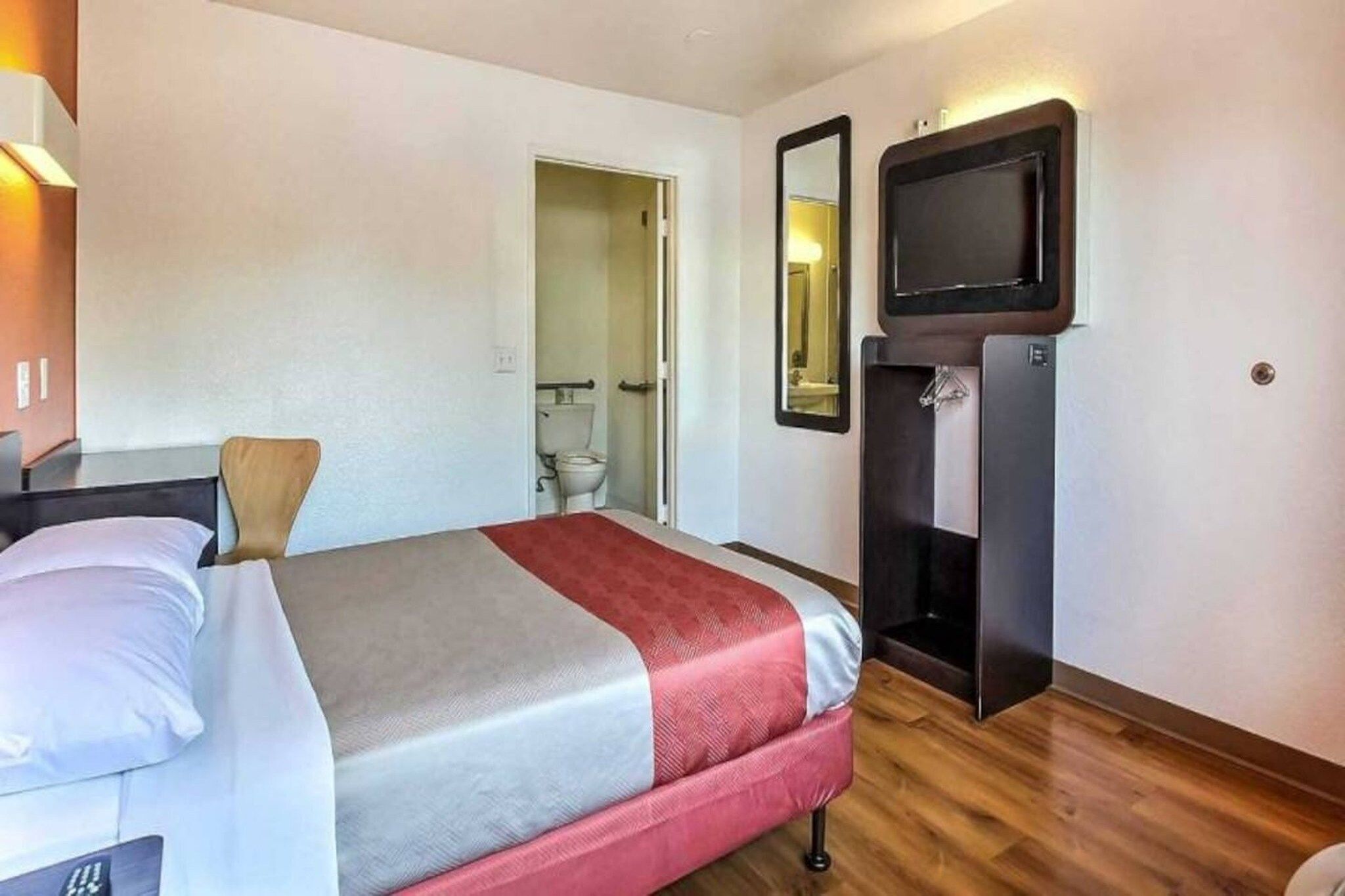 Una habitación de hotel con cama, una silla, televisión y espejo.