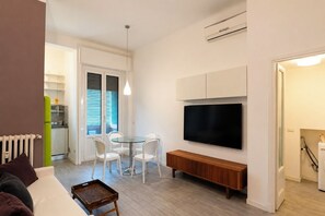 A modern living room with a flat-screen TV, a dining area with chairs, and a kitchen in the background. - Argonne Apartment - Corsica (Milano)